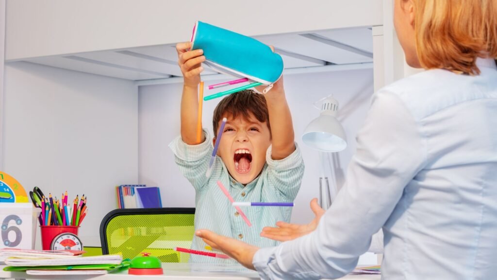 Niño haciendo un berrinche y lanzando sus útiles escolares mientras un adulto intenta calmarlo